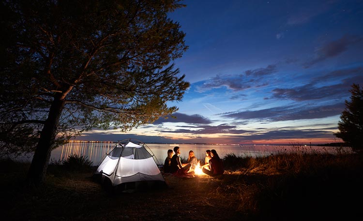 Ungdomar tältar vid en sjö och sitter upp på kvällen och pratar vid en eld