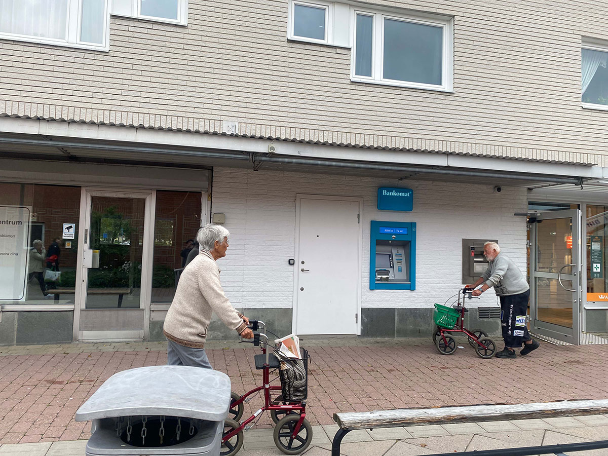 Hallstavik centrum med bankomat och två pensionärer som med rullator som går genom stan.