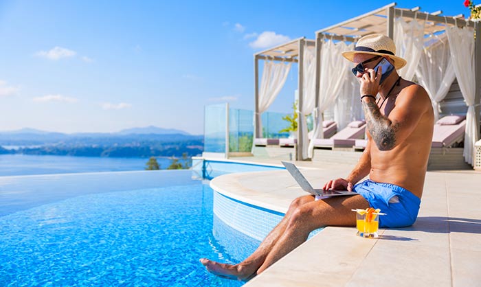 Man sitter i babyxor vid en pool med laptop och en drink och jobbar online för att tjäna pengar