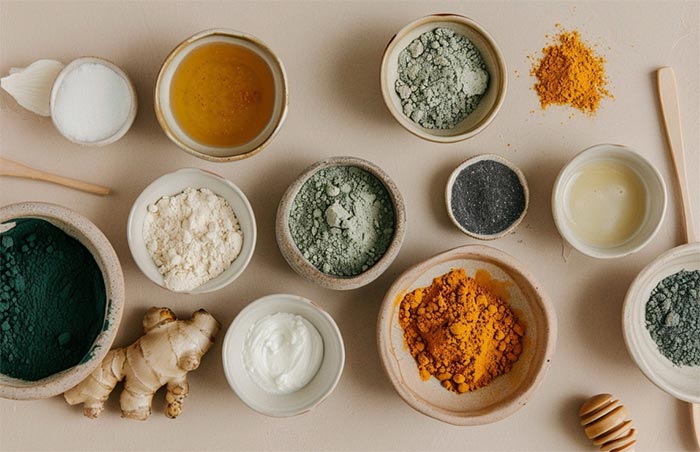 Skålar på ett bord men olika pulver i med kreatinmonohydrat, rot av ingefära, svartpeppar, spirulina, ashwagandha, gurkmeja och kollagenpulver.