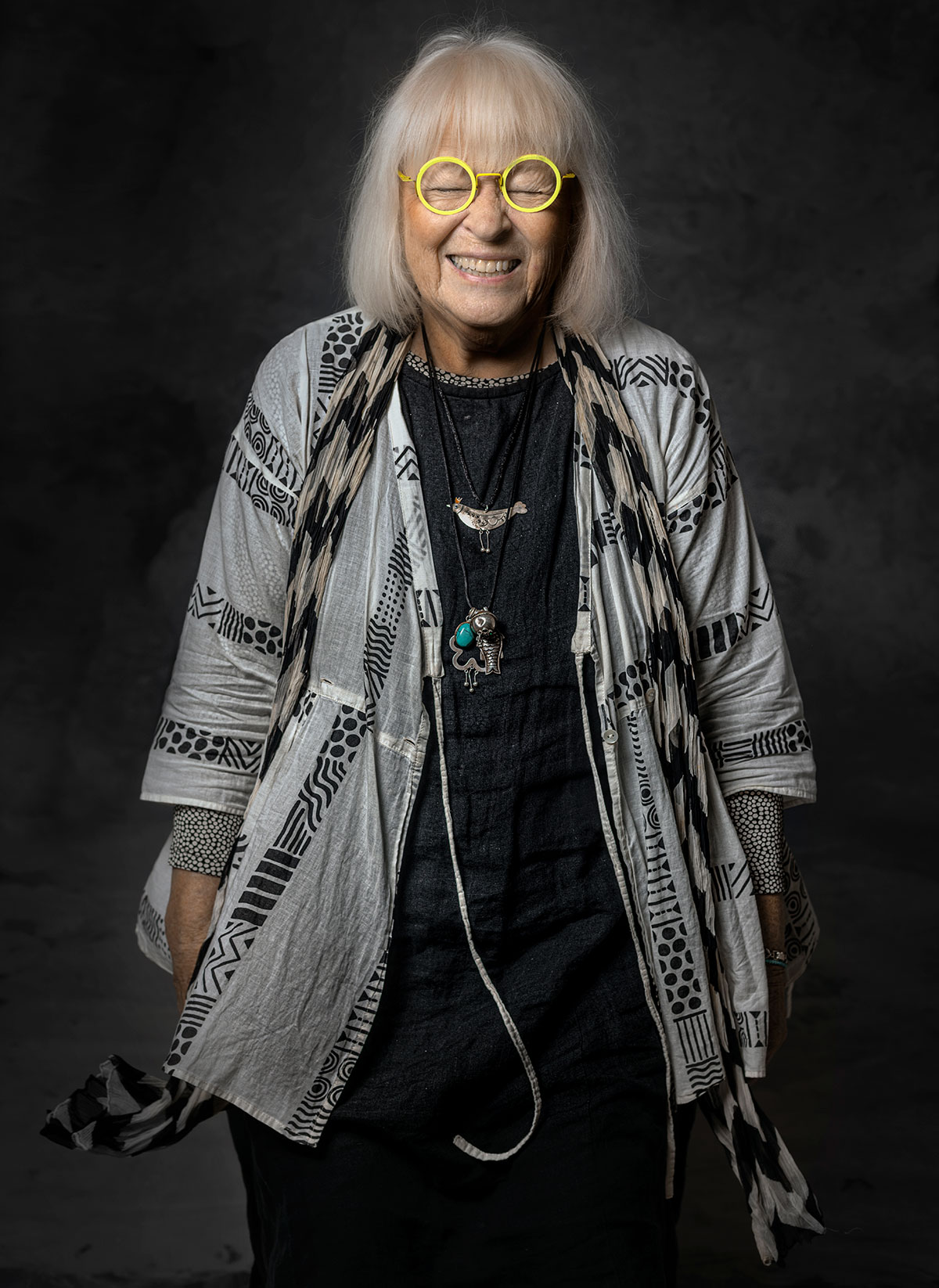 Gudrun Sjödén med gula glasögon i porträtt mot mörk bakgrund, fotograferad av Niklas Palmklint.