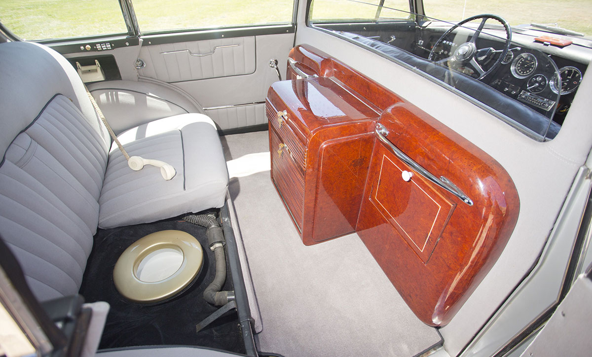 Baksätet i en Rolls-Royce från 1954, uppfällt så att en toalett med guldfärgad sits syns. Bredvid finns en telefonlur och ett skåp i rotfanér.