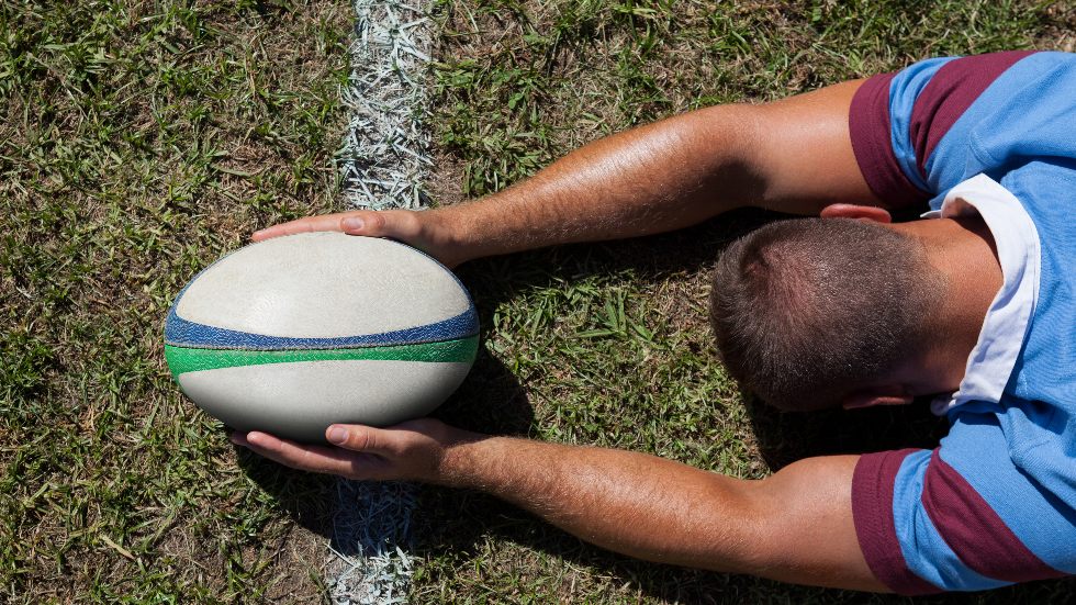 Liggande rugbyspelare håller bollen vid mållinjen