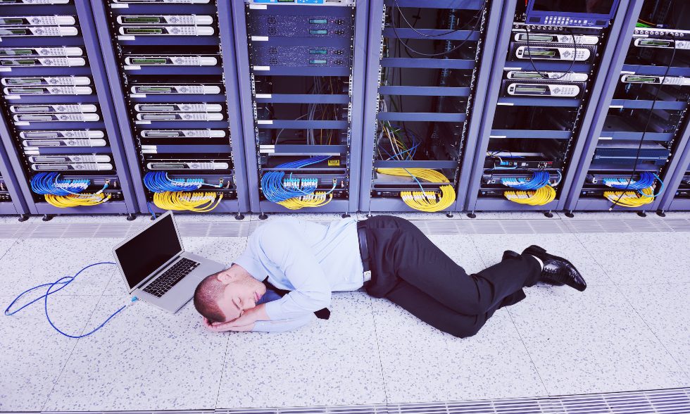 Foto: Envato/Dotshock – en utmattad man sover på golvet vid sin dator i ett serverrum